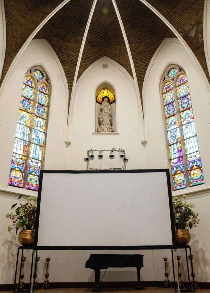 De Kerkzaal met projectiescherm, glas-in-loodramen en vleugel