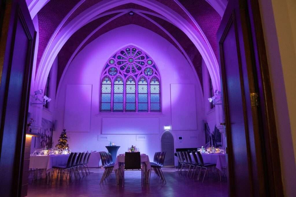 De Kapittelzaal in paars licht met gedekte tafels en kerstboom, gezien door de open deuren