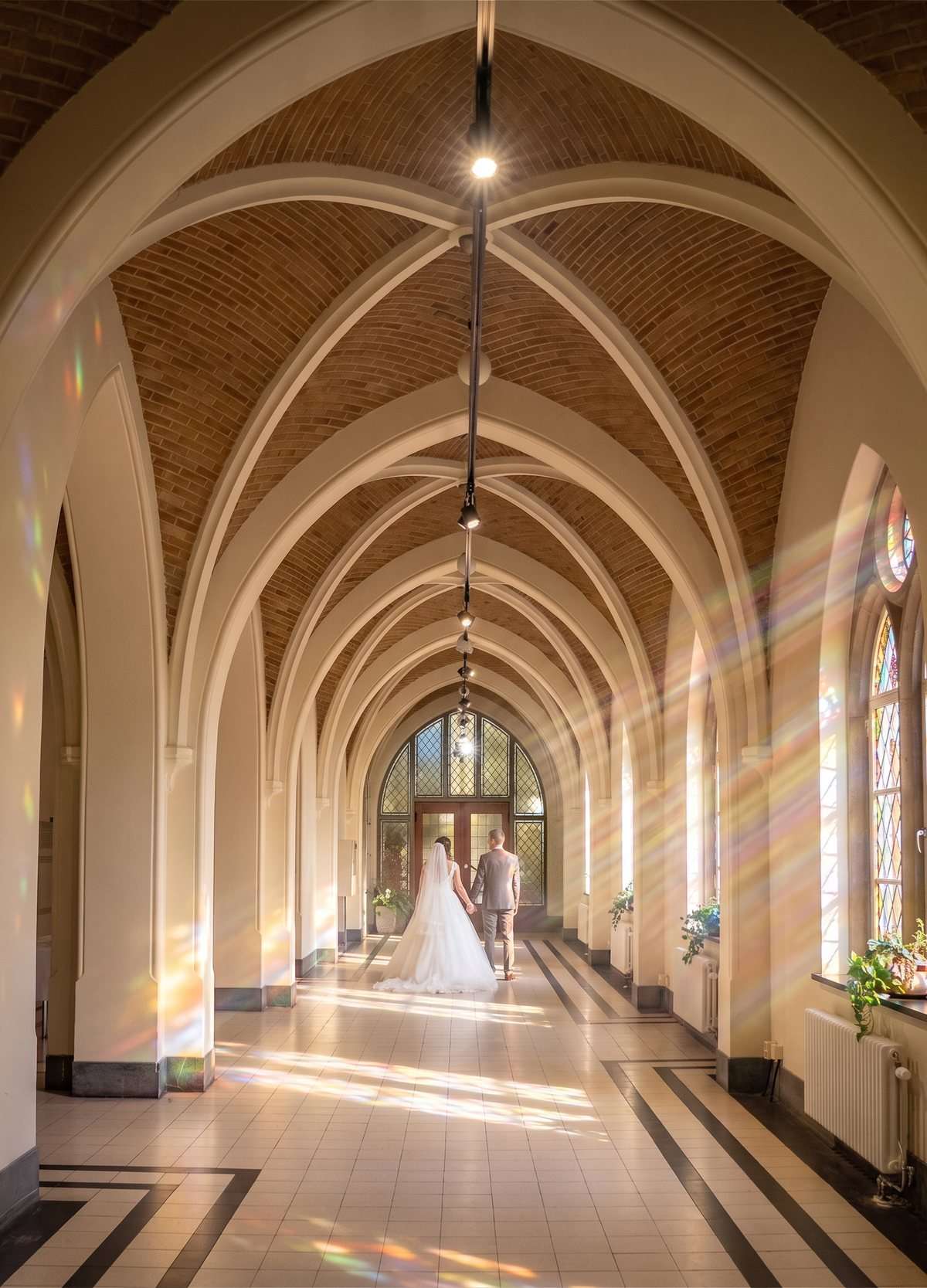 Een bruidspaar loopt door de Foyer, met zonlicht door het glas in lood op de vloer