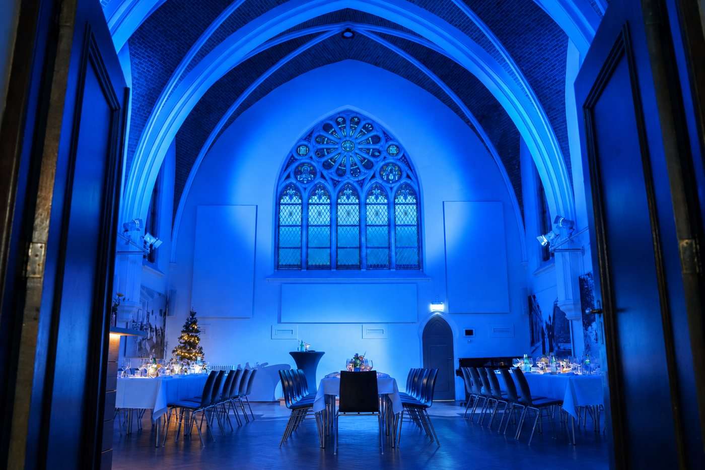 De Kapittelzaal van Hemels in blauwe verlichting, met het rozetraam en gedekte tafels