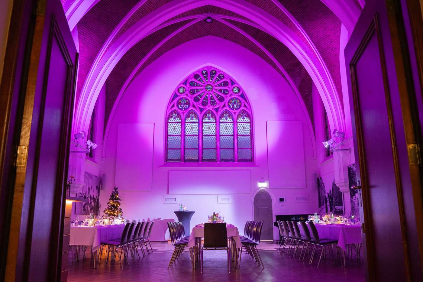 De Kapittelzaal van Hemels in roze verlichting, met het rozetraam en gedekte tafels
